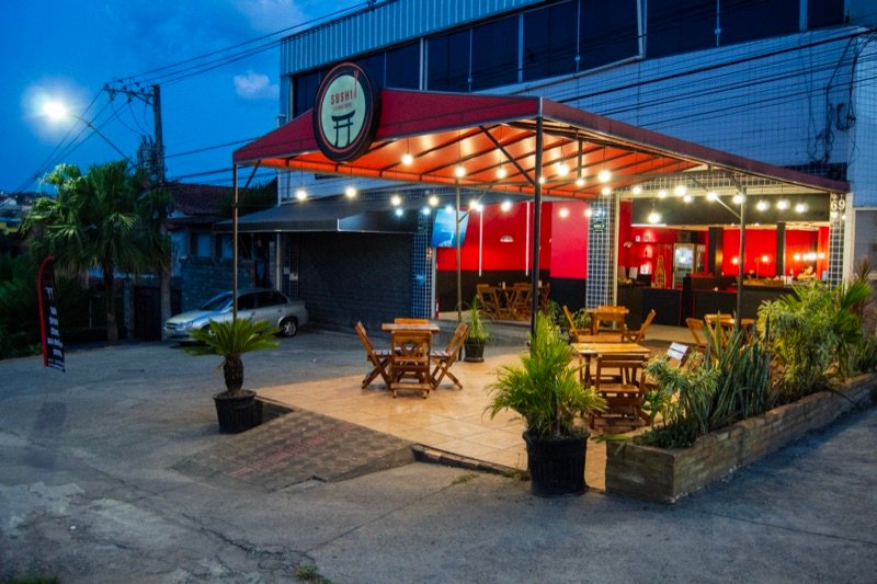 Área externa do restaurante à noite, com cobertura laranja e luzes penduradas