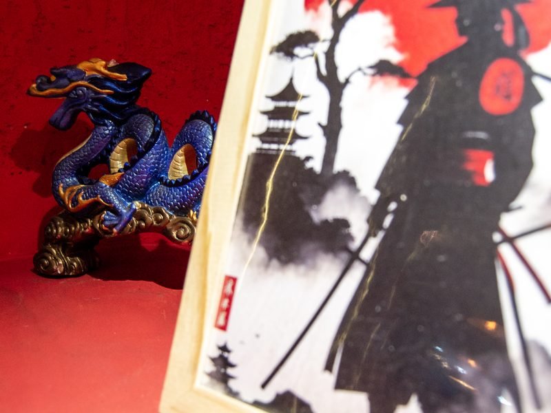 Peça decorativa de dragão azul e quadro com ilustração de samurai em ambiente vermelho