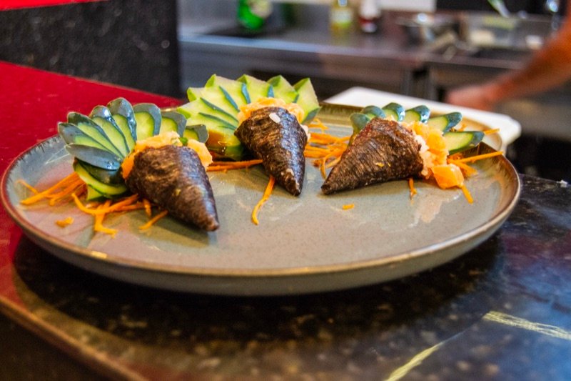 Temakis servidos em prato cinza, com pepino fatiado e cenoura ralada