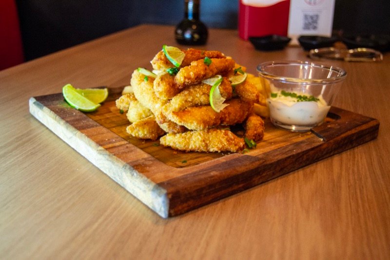 Iscas de peixe empanadas e crocantes, com limão e molho tártaro, em tábua de madeira